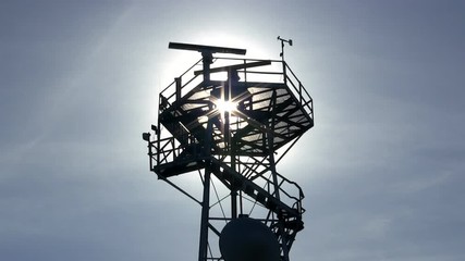 Marine traffic control radar tower silhouette with spinning antenna, anemometer and wind direction sensors against blue sky and wispy clouds - Powered by Adobe