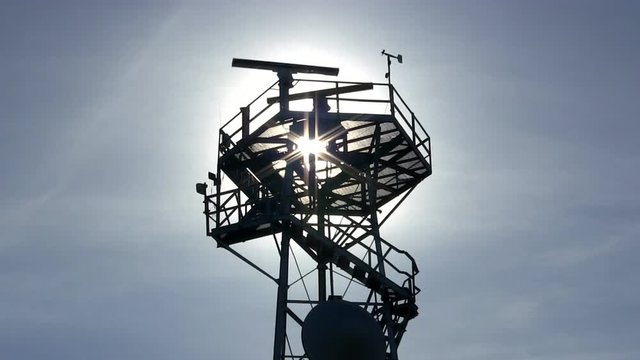 Marine traffic control radar tower silhouette with spinning antenna, anemometer and wind direction sensors against blue sky and wispy clouds - Powered by Adobe