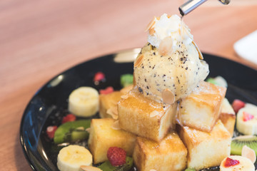 Honey toast wiht mix fruits in the black dish place on the wooden table in the coffee shop in selective focus.
