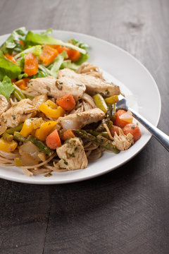  
Whole wheat pasta with cooked chicken and vegetables including carrots, bell peppers, onion, and asparagus with a small salad as a side cropped off shot
