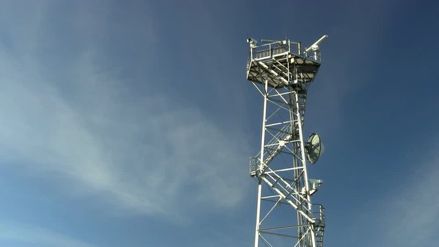 Radar tower long shot of spinning antennas and surveillance camera against blue sky and wispy clouds
