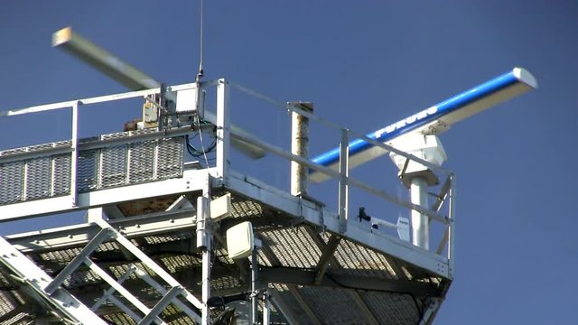 Radar close-up of spinning antennas on marine traffic control tower against blue sky