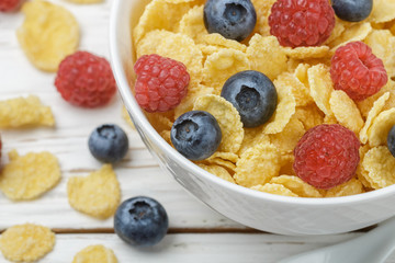 Cornflakes with fresh berries raspberry and blueberry in white bowl on the table. Healthy Breakfast. Selective focus. Top view