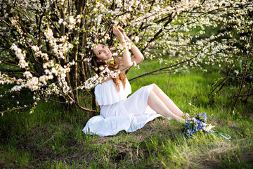 Beautiful girl with long hair in a white dress in a flowery garden with flowers