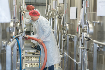 Factory operators connecting hose to vat