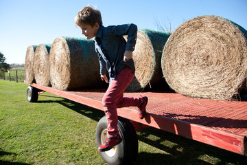  Boy jumping off the side of a farm tractor trailer with bales of hay.