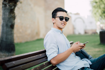Obraz premium Handsome asian Man using cellphone on a bench in the park