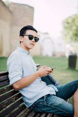 Casual happy asian  man using a smartphone sitting on a bench in a park