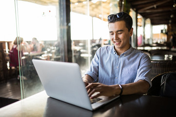 Obraz premium Portrait of handsome asian smiling man using laptop in the cafe