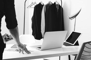 Fashion designer talking mobile phone and using laptop with digital tablet computer in modern studio