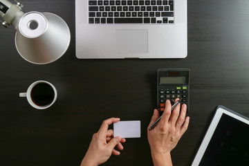 Internet shopping concept.Top view of hands working with calculator and laptop and credit card and tablet computer on dark wooden table background