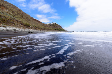 Line of foam formed by waves on the black sand beach of the Almaciga in Tenerife, Canary Islands.