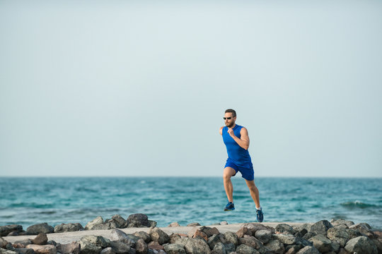 Man runner with handsome face running along stone coast