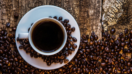 Coffee. A hot cup of coffee and roasted coffee beans on a wooden table. Dark background
