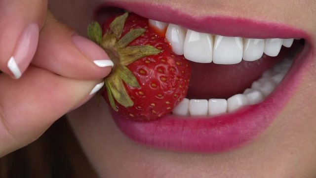 Slow motion close up: The young girl bites a strawberry. Minimally invasive porcelain veneers/ smile/ porcelain veneers color bleach 1