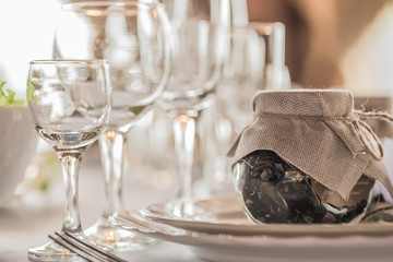 Rustic table setting for a wedding celebration in nice cozy restaurant. Wineglasses, plates and food on a table. Guests complement in a rustic jar
