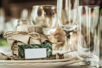 Rustic table setting for a wedding celebration in nice cozy restaurant. Wineglasses, plates and food on a table. Guests complement in a rustic jar. Nice card with a space for text
