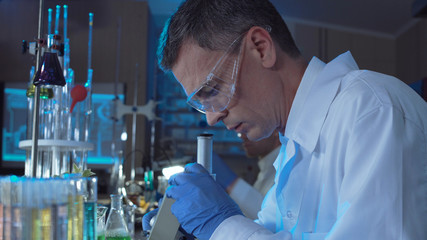 Side view of adult man in white gown and glasses watching in microscope while working in lab.
