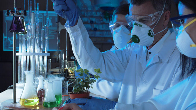 Three People In Protective Suits Using Dropper And Chemical And Conducting Experiment In Laboratory.