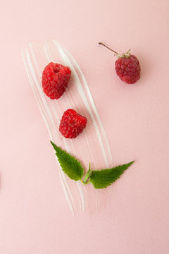 Ripe raspberries, green mint leaves and a smear of sour cream on a pastel pink background..