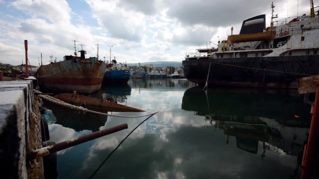 Sea Port. Ships Staying in Bay. Old Fish Boats in Dock. Rope Hanging. Rust Metal. Stone Embankment. Cloudy Sky Reflection on Dark Water. Summer Day
