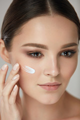 Beauty Cosmetics. Woman Putting Cosmetic Cream On Beautiful Face