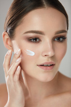 Beauty Cosmetics. Woman Putting Cosmetic Cream On Beautiful Face