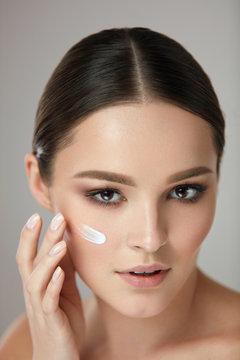Beauty Cosmetics. Woman Putting Cosmetic Cream On Beautiful Face