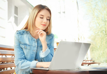 Young girl sitting on bench and using laptop outdoors
