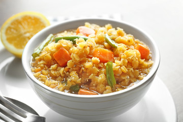 Bowl with tasty lentil porridge and vegetables on table, closeup