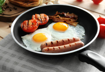 Frying pan with tasty eggs, sausages and tomatoes on table