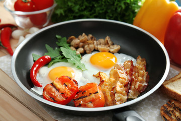Frying pan with tasty eggs, bacon and tomatoes on table