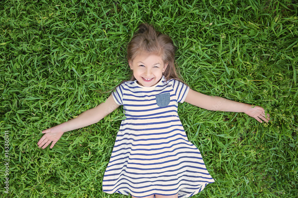 Wall mural Cute little girl lying on green grass in park