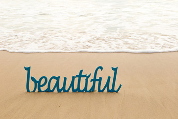 Beautiful - blue wooden word in sand with waves on beach