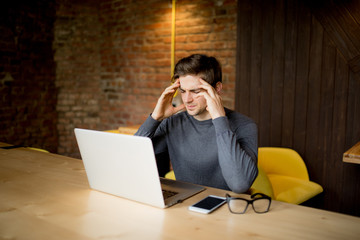 Handsome young man working at laptop with sad face or head ache  working at laptop