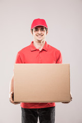 Young smiling delivery man with box in hand in red uniform on white background