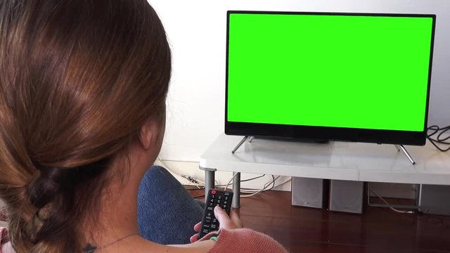 Woman Using Television Remote In Green Screen Close Up Shot. Young Woman watching television with green screen, shot behind models shoulders