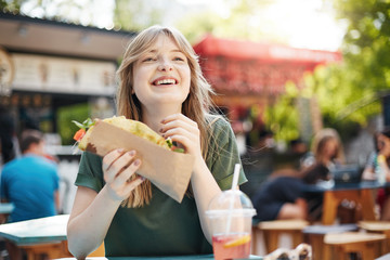 Girl eating taco. Hungry freckled blonde woman holding junk food on a food court on a sunny summer...