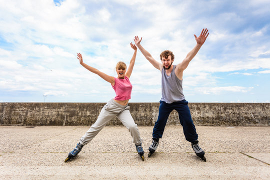 Two people on rollerblades with spread arms.