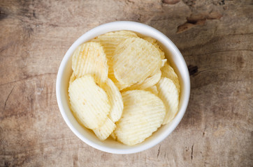 Potato chips in a bowl on wooden background