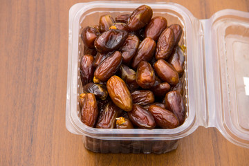 Dried date fruits in plastic container on wooden table
