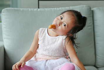 Fototapeta premium Little girl eating sausage on the sofa.
