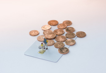 Miniature shoppers with shopping cart figure on a credit card or debit card and a pile of coins background using as shopping, e-commerce and online business concept.