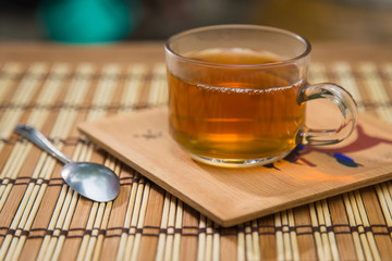 Glass cup of tea, teaspoon on wooden table.