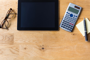 Work desk with tablet, glasses, calculator and notepad on wooden table