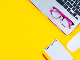 office accessories including calculator, mouse laptop, glasses, red pencil and note book on yellow background. Education and business concept.