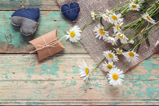 Bouquet of daisies with gift box and denim hearts on old wooden background. Place for text.