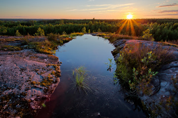 Sunset summer scene with a small pond on the hilltop in Finland