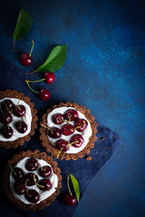Chocolate tarts with cream and fresh berries of sweet cherry on a dark concrete background. Selective focus.Top view.