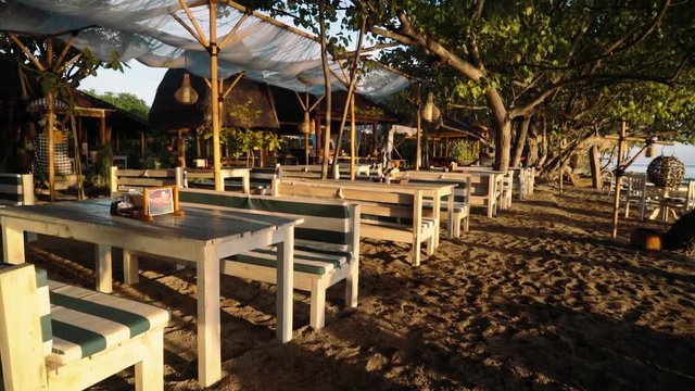Beachside restaurant with wooden benches and tables on sunrise, Bali